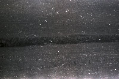 B&W photographic paper exhibiting extensive scratches, dust, and faint, blurred vertical lines. Likely a test print or damage...