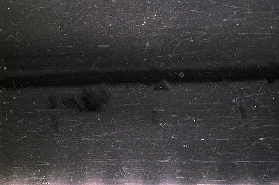 Abstract image showcasing a dark, textured surface with prominent dust and scratch artifacts. The horizontal line suggests a ...
