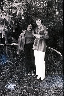 Two women in a casual outdoor portrait, circa 1970s. One wears a dark sweater & denim jacket, the other a patterned dress & w...