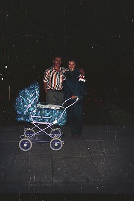Two men stand beside a vintage, ornate baby carriage, likely in a residential area during rainy weather. The man on the left ...