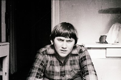 Close-up, black & white portrait of a young man with short, dark hair, wearing a plaid shirt. Interior setting with simple fu...