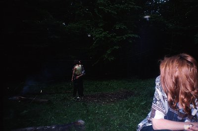 A person stands on a patch of grass, partially obscured by foliage, as viewed from a low angle. The subject wears a striped s...