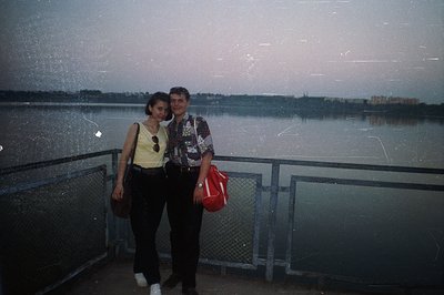 A young couple poses on a promenade overlooking a wide, calm body of water, likely the Black Sea. The woman wears a yellow ta...