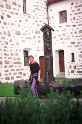 A person in athletic wear stands near a stone monument in a courtyard. The monument features a carved relief sculpture within...