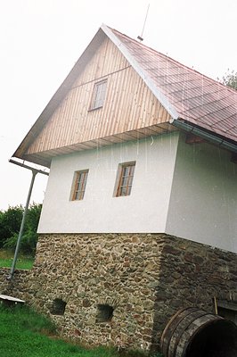 Stone base supports a whitewashed upper section with a wooden-shingled roof, characteristic of Alpine architecture. Rain fall...