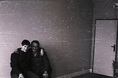 A seated man, with a younger person beside him, is captured in a stark, interior scene. The subjects are tightly framed again...