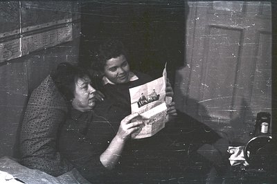 Two individuals, appearing to be a mother and child, intently examine a photograph. The mother wears a patterned dress, while...