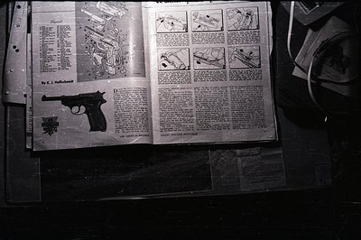 A detailed technical article about the Heckler & Koch P7 pistol is open on a dark surface, showcasing exploded diagrams and t...