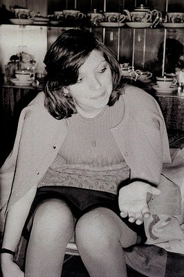 A young woman sits, holding a baby, in front of a display of china. She has short, dark hair and is wearing a patterned top. ...