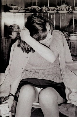 A young woman with a short, layered hairstyle sits hunched, appearing distressed, her face buried in her hands. She wears a s...