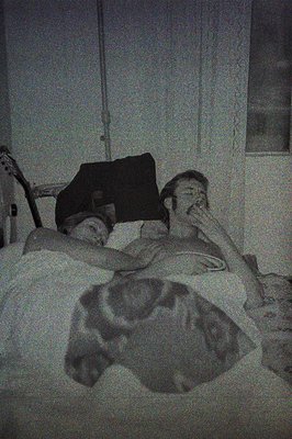 A black and white image shows a person lying in a bed with a dog. The person is facing upwards, covering their face with thei...