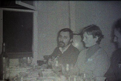 A black and white photo captures two seated individuals at a table setting, likely during a meal. The man, with a beard, look...