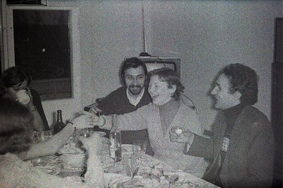 A candid monochrome shot shows three men at a table, enjoying what appears to be a casual gathering. Visible table setting in...