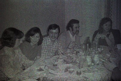 Group gathers around a table laden with food and drink, exhibiting a vintage aesthetic. Five individuals, four women and one ...