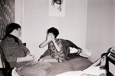 Three young people in a casual interior setting. A man sits in a chair, facing two individuals reclining on a daybed. The wom...
