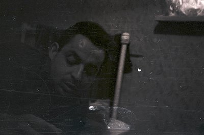 Close-up portrait of a man in shadow, likely 1960s or 70s. Strong lighting creates dramatic contrast; a long, thin object (po...