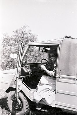 A woman in sunglasses drives an off-road utility vehicle, likely a Toyota Land Cruiser. She appears relaxed, positioned withi...