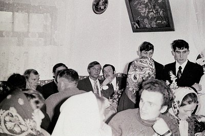 Group portrait at a gathering; men in suits and sweaters, a woman in traditional floral headwear, likely a wedding or formal ...