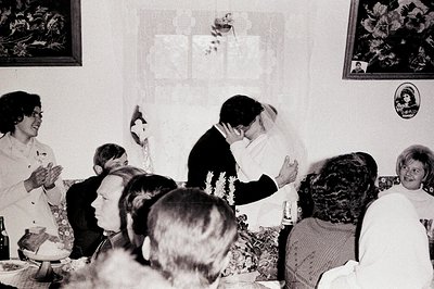 A bride and groom share a kiss during a wedding reception. Guests seated at a long table watch and applaud, captured in a can...