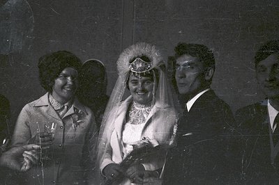 Black & white portrait of a couple at their wedding. Bride wears a veil and floral headpiece, groom in a suit. Guests are vis...