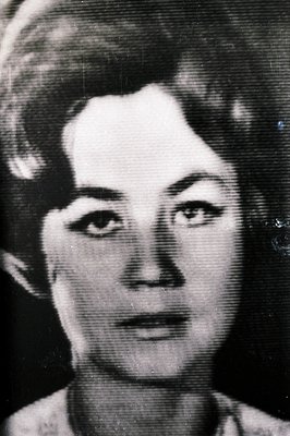 Close-up portrait of a woman with styled hair and defined eyebrows. The image exhibits visible grain and wear consistent with...