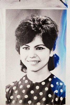 Portrait of a woman with a stylish, textured bob haircut and a joyful smile. She wears a white top with a dark polka dot patt...