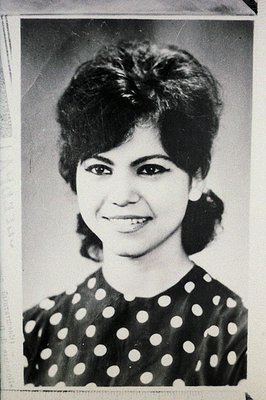 Black and white portrait of a young woman with a stylish, layered hairstyle and defined eyebrows. She wears a dark top with w...