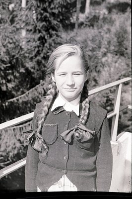 Head and shoulders portrait of a young girl with braided hair, wearing a dark, collared dress adorned with a decorative bow. ...
