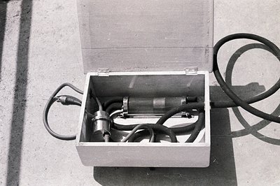 Open wooden box containing what appears to be scientific or industrial equipment: a vacuum tube, cables, and connectors. Like...