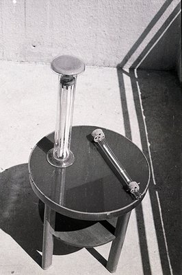 A close-up captures a black, round table with a cylindrical glass object and a metallic tool. Strong directional lighting cre...