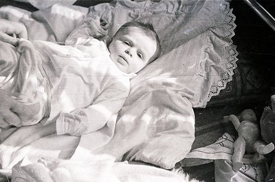A monochrome portrait features a baby nestled in a wicker cradle. The child wears a button-down shirt and appears to be sleep...