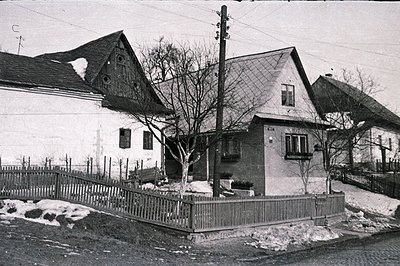 Exterior view of two traditional homes with steeply pitched roofs and weathered facades. A wooden fence separates the propert...