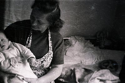 A woman tenderly holds an infant, likely a baby, in a domestic setting. Visible clothing suggests a casual, informal moment. ...