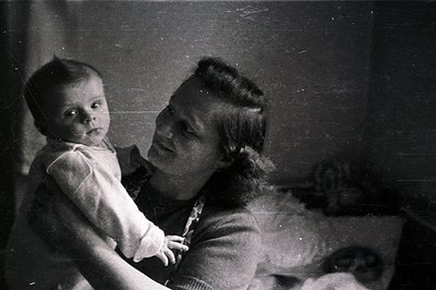 A monochrome image captures a woman holding a baby. The woman is in profile, with a gentle smile visible, while the infant ga...