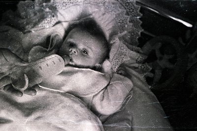 Infant being fed with a bottle, likely formula. The vintage photograph exhibits visible scratches and dust, common to early p...