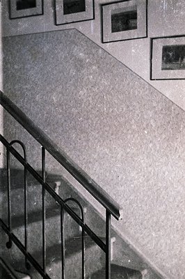 A grayscale image captures a section of an interior staircase with black metal railings and a smooth, curved banister. Three ...