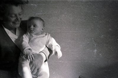 A smiling woman cradles an infant in a simple, intimate pose. The grayscale image shows a shallow depth of field, blurring th...