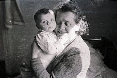 A young mother cradles a baby close, both with expressive faces. The image, likely a personal snapshot, captures a tender mom...