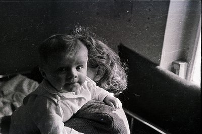 A young child with tousled, curly hair sits on a lap, facing the camera. The image, captured in black and white, shows a simp...