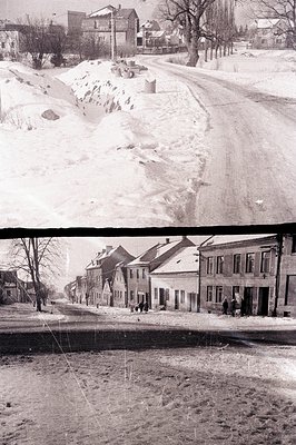 A monochrome street view depicting a line of buildings with ornate facades. Snow covers the elevated ground on the left, tran...