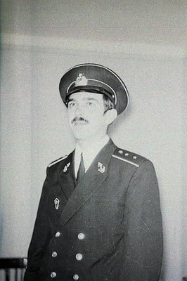 Formal portrait of a man in a dark military uniform with a peaked cap and prominent mustache. Detailed insignia on collar and...