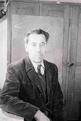 A seated portrait of a middle-aged man in a corduroy suit, vest, and tie. He presents directly to the camera with a serious e...