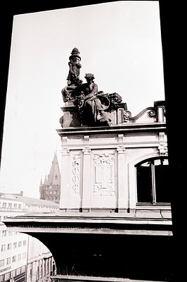 Architectural detail of a building facade featuring a statue of a figure with an ornate column and decorative relief carvings...