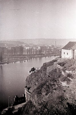 A view of a river landscape with a stone building on a cliffside. The scene features a dark body of water, likely a river or ...