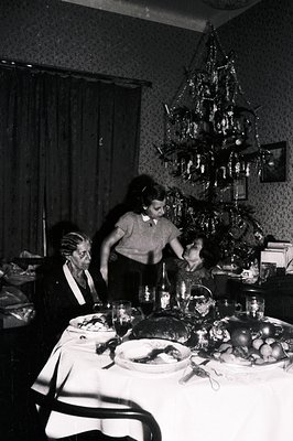 A candid moment captures a festive indoor scene – possibly a holiday gathering. A formally dressed older woman stands near a ...