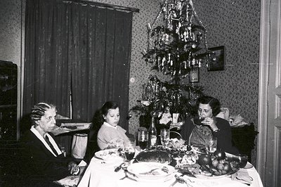 A family gathers around a laden table during a festive occasion, likely Christmas. A young girl sits between an older man in ...