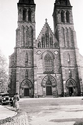 Imposing Gothic Revival cathedral with twin towers, showcasing intricate stonework and pointed arches. A vintage automobile a...
