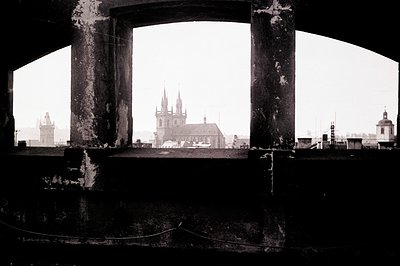 A framed view through a weathered archway showcases a historic cityscape. Note Gothic architecture with prominent spires & ro...