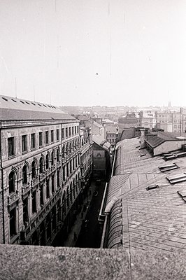 High-angle, monochrome view of a wide, bustling street lined with elaborate, late 19th-century buildings. Note the detailed a...