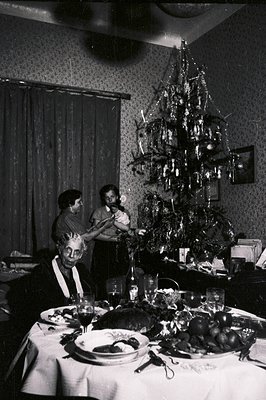 Festive holiday gathering: a formally dressed man sits at a laden table with a woman and a young child. A fully decorated Chr...